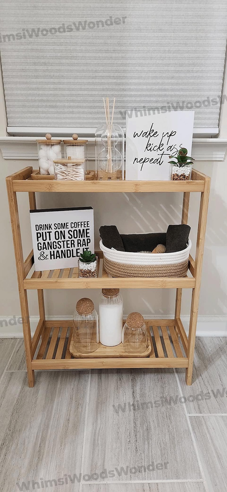Puede incluir: Una estanter&iacute;a de bamb&uacute; de tres niveles con un cartel blanco que dice "wake up kick ass repeat" y un cartel blanco y negro que dice "Drink some coffee put on some gangster rap & handle it". La estanter&iacute;a est&aacute; llena de varios art&iacute;culos, incluyendo bolas de algod&oacute;n, bastoncillos de algod&oacute;n, un frasco de vidrio con palitos, una peque&ntilde;a planta en maceta, una cesta tejida en blanco y negro y tres frascos de vidrio con tapas de corcho.