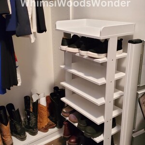 May include: White shoe rack with six shelves, filled with shoes. The rack is in a closet with a white wall and a wooden floor. The text "WhimsWoodsWonder" is visible on the rack.