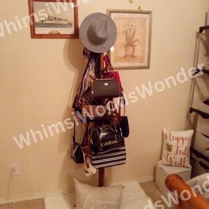 May include: A wooden coat rack displaying a gray fedora, various handbags, and a leopard print scarf. The rack is adorned with several purses in different styles and colors, including black, pink, and white. Two framed pictures hang on the wall.
