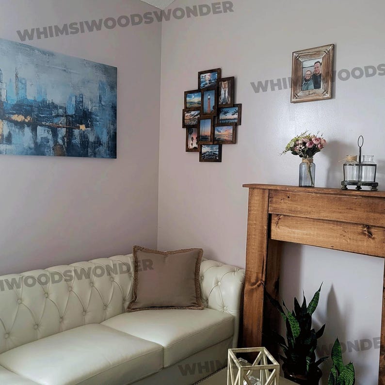 May include: A white leather sofa with a brown pillow in front of a fireplace mantel with a picture frame collage on the wall above it. The fireplace mantel is made of wood and has a rustic look. There is a plant in a pot on the floor in front of the fireplace.