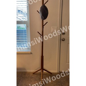 May include: A tall, wooden coat rack with a dark gray hat hanging from one of its pegs. The rack has a tripod base and multiple pegs for hanging coats or hats. The rack is made of a light brown wood.
