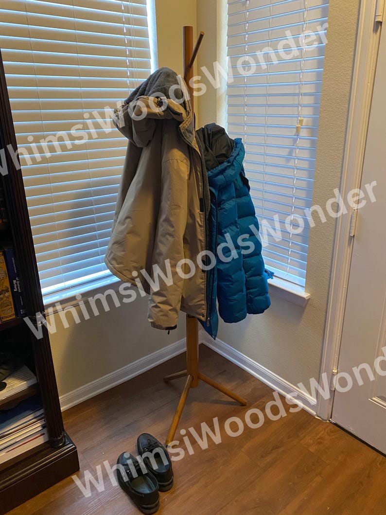 May include: A wooden coat rack with three coats hanging on it. The coats are tan and teal. Two pairs of black shoes are on the floor in front of the coat rack. The background includes a window with blinds and a door.