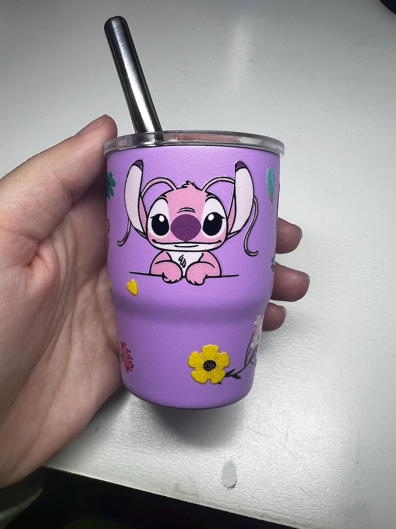 Puede incluir: Un vaso morado con un personaje de dibujos animados, una pajita plateada y decoraciones florales. El vaso est&aacute; dise&ntilde;ado para bebidas fr&iacute;as. El vaso mide unos 10 cm de alto.