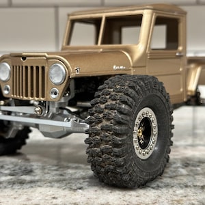 Könnte beinhalten: Ein goldfarbener, vintage-artiger Pick-up mit schwarzen Reifen und einem detaillierten Kühlergrill. Der Wagen hat ein schwarzes Interieur und ein schwarzes Lenkrad.