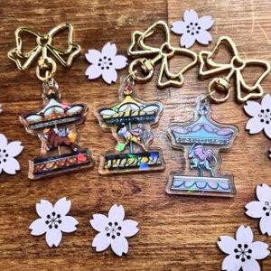 Op de afbeelding: Drie kleurrijke carrouselpaardcharms met gouden strik-sleutelhangers. Elke charme heeft een ander paardontwerp met een glinsterende achtergrond. De charms zijn perfect om een vleugje whimsy toe te voegen aan je sleutels, tassen of andere accessoires.