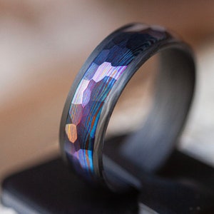 May include: A black and iridescent ring with a hammered finish. The ring has a textured surface and a wide band.