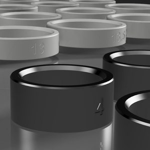 Könnte beinhalten: Ein Satz schwarzer und grauer Ringe mit aufgedruckten Zahlen. Die Ringe sind aus einem glatten, harten Material gefertigt und werden wahrscheinlich zum Größen- oder Messen verwendet.