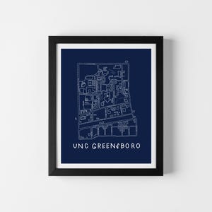 Op de afbeelding: Ingelijste print met een gedetailleerde witte lijntekening van een kaart op een marineblauwe achtergrond. De tekst "UNC GREENSBORO" staat onderaan. De print zit in een zwart frame, ideaal voor wanddecoratie, in cm.