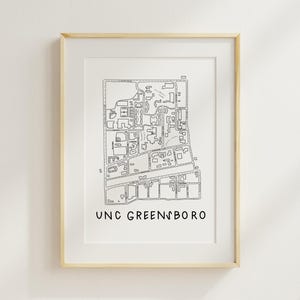 Op de afbeelding: Een ingelijste zwart-wit lijntekening van een kaart van UNC Greensboro. De kaart toont gebouwen, wegen en groene ruimtes. De tekst "UNC GREENSBORO" is in een eenvoudig lettertype onderaan de afbeelding gedrukt.