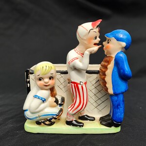 May include: A ceramic figurine set of three baseball players. The players are wearing red, white and blue uniforms. The figurine is a vintage style and is perfect for a baseball fan.