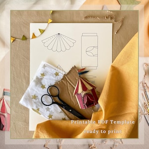 May include: A still-life image featuring a printable PDF template with circus-themed designs. The composition includes a sheet with line drawings, a small circus tent, scissors, and fabric. The text "Printable PDF Template ready to print" is visible.