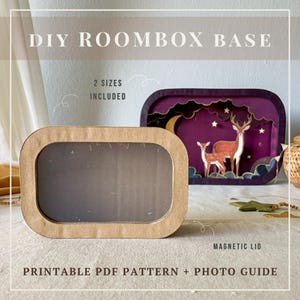 May include: A DIY roombox base kit featuring a rectangular cardboard frame with a clear window and a magnetic lid. The text reads DIY ROOMBOX BASE, 2 SIZES INCLUDED, MAGNETIC LID, and PRINTABLE PDF PATTERN + PHOTO GUIDE. A finished purple diorama with deer is visible.