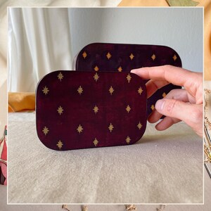 May include: Two rectangular boxes with rounded corners featuring a deep burgundy finish and a repeating pattern of small gold-colored four-pointed stars. The boxes are stacked slightly, with the smaller one positioned in the foreground.