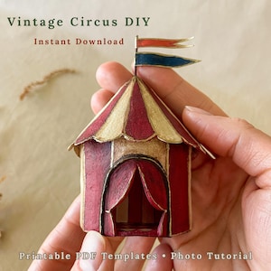 May include: A miniature circus tent model featuring red and cream vertical stripes, a scalloped roof edge, and a dual-coloured flag topper in red and blue. The text Vintage Circus DIY, Instant Download, Printable PDF Templates, Photo Tutorial is visible.