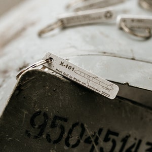 May include: A silver keychain with a small metal tag that reads "X-101 that fell in Kyiv on January 2023". The tag has a small drawing of a missile on it.