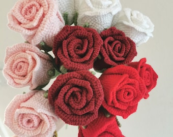 May include: A bouquet of crocheted roses in shades of white, pink, and red. The roses are arranged in a hand-held bouquet.