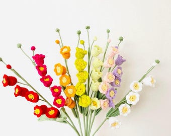 May include: A bouquet of colorful, crocheted flowers in shades of red, orange, yellow, green, pink, purple, and white. The handmade flowers have green stems and leaves, held in a hand against a white background. The flowers are a mix of different shapes and sizes.