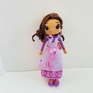 May include: A crocheted doll with brown hair, a purple dress, and pink shoes. The doll has a brown face and large black eyes.