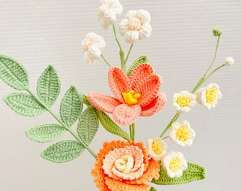May include: A bouquet of crocheted flowers in shades of peach and white. The bouquet includes a large peach rose, a smaller peach flower with five petals, and several small white flowers with yellow centers. The flowers are attached to green crocheted stems and leaves.