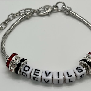 May include: A silver charm bracelet with a heart charm and a charm that spells out "DEVILS" in white letters with black outlines and red and black crystal accents.
