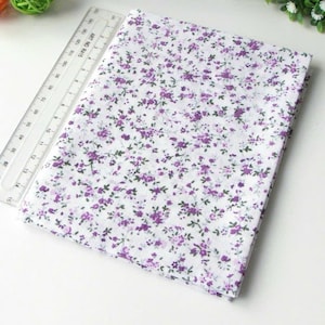 May include: A folded piece of white fabric featuring a small purple floral pattern with green stems. A clear plastic ruler is placed alongside the fabric, showing a measurement scale that extends up to 15 inches in length.