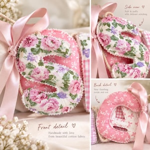 May include: A fabric letter S with a pink and white floral pattern, featuring a scalloped edge and a light pink satin ribbon tied to the side. The letter is soft and puffy with visible stitching, and the back shows a pink and white gingham fabric.