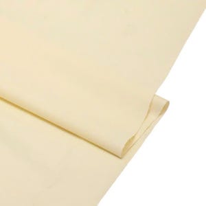 May include: A single sheet of light cream-colored fabric folded over itself. The material has a smooth, matte surface with a consistent, solid color throughout. The fabric is draped to show a soft, clean edge and a simple, uniform texture.