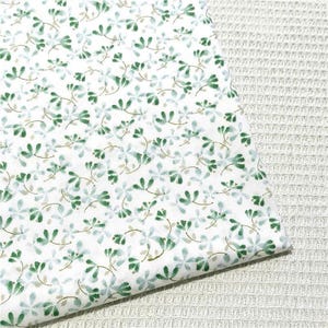 May include: A white fabric featuring a repeating pattern of small, delicate green and light blue floral sprigs. The design consists of tiny leaves and stems scattered across the surface, creating a soft, botanical appearance on the textile.