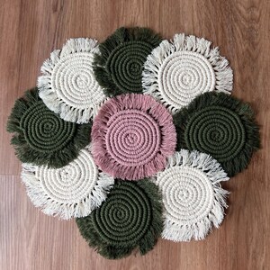 May include: A set of eight round crocheted coasters in white, green, and pink. Each coaster has a fringe border and a circular pattern in the center.