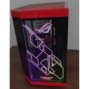 Peut inclure: Un boîtier d'ordinateur rouge et noir avec un panneau latéral en verre. Il présente un motif géométrique lumineux et le texte "REPUBLIC OF GAMERS". Les bords supérieur et inférieur sont rouges.