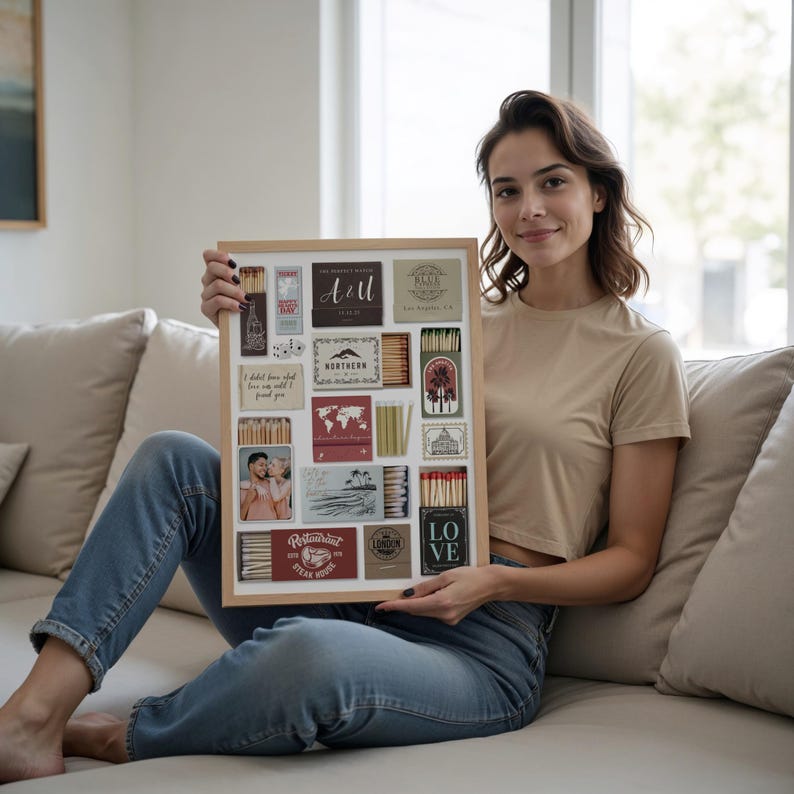 May include: A framed collage featuring various matchbox designs, including the word "ART" and the word "LOVE". The matchboxes have different colors and designs, with some featuring text and images. The frame is made of light-colored wood.