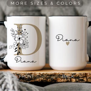 May include: White ceramic mug with a black handle. The front of the mug features a gold letter "D" with black floral designs and the name "Diana" written below. The back of the mug has the name "Diana" written in cursive with a small gold heart.