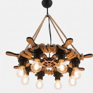 May include: A nautical-themed chandelier with a wooden ship's wheel design. The light fixture has eight light bulbs, brown rope, and wooden accents. The chandelier hangs from a black ceiling mount.