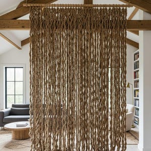 May include: A brown rope curtain suspended from a wooden beam, serving as a room divider. The curtain is constructed from thick, twisted ropes, introducing a natural, rustic aesthetic. The ropes are arranged vertically, providing a visual separation within the space.