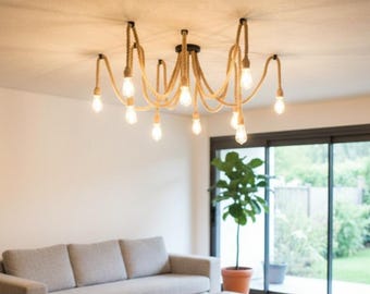 May include: A rustic chandelier with a natural rope design. The light fixture has multiple light bulbs hanging from the ceiling. The chandelier is suspended above a gray sofa and a potted plant.
