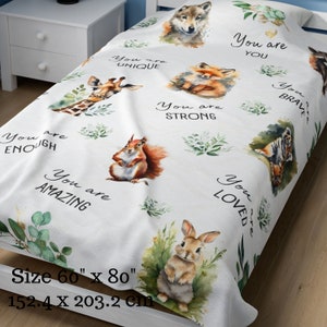 May include: White throw blanket with a watercolour design featuring various animals, including a wolf, fox, giraffe, squirrel, rabbit, and tiger. The blanket has the text "You are" repeated throughout with different words following, such as "unique", "strong", "enough", "amazing", "loved", and "brave". The blanket measures 152.4 cm by 203.2 cm.