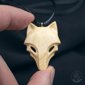 Pode incluir: Um colar com um pingente de madeira em forma de raposa com um cordão de couro preto. O pingente é esculpido em uma forma estilizada com um design simples.