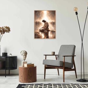 May include: A framed print depicts a figure kneeling in prayer, bathed in light. The artwork, with a warm color palette, is displayed on a white wall above a mid-century modern chair. The room is decorated with minimalist furniture and decor.