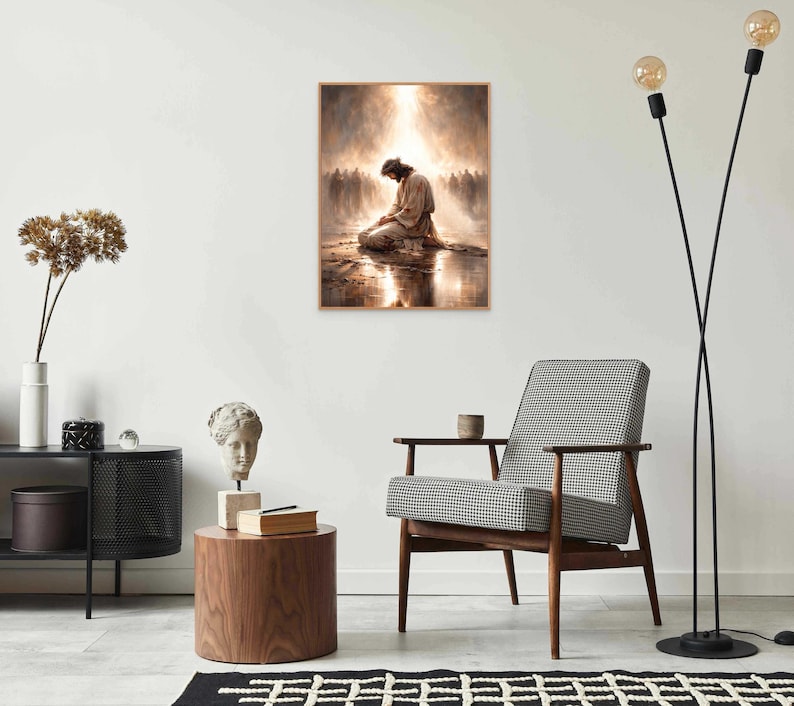 May include: A framed print depicts a figure kneeling in prayer, bathed in light. The artwork, with a warm color palette, is displayed on a white wall above a mid-century modern chair. The room is decorated with minimalist furniture and decor.