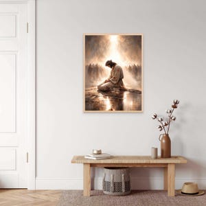 May include: A framed print depicts a figure in a robe kneeling in prayer, bathed in light. The artwork features a soft, warm color palette with a crowd of figures in the background. The image evokes a sense of spirituality and reverence.