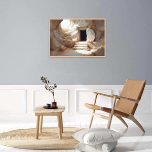 May include: A painting of a stone tomb with a large stone rolled away, revealing a dark opening. The tomb is lit by a bright light coming from the opening. The painting is framed in a light wood frame.