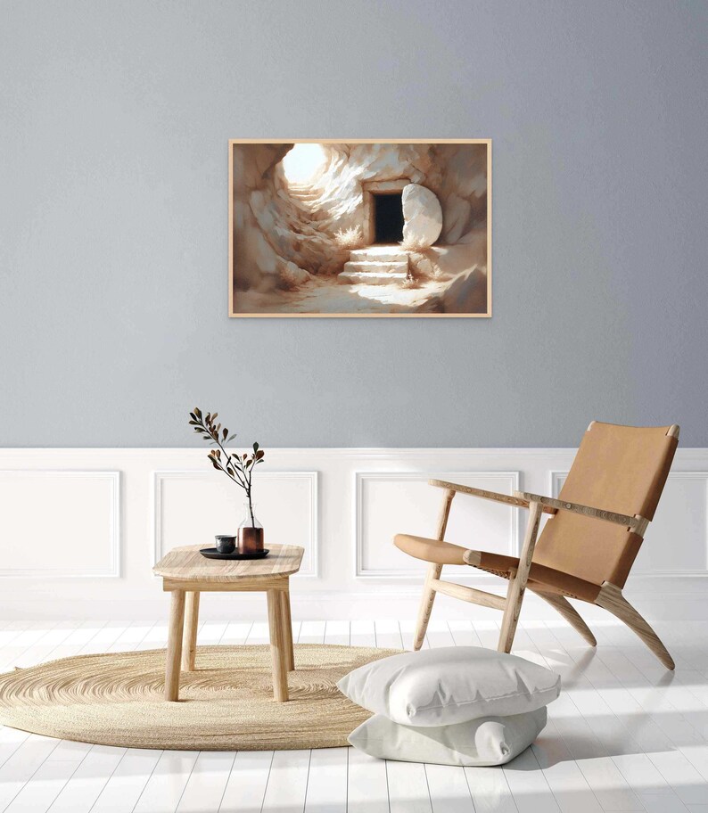 May include: A painting of a stone tomb with a large stone rolled away, revealing a dark opening. The tomb is lit by a bright light coming from the opening. The painting is framed in a light wood frame.