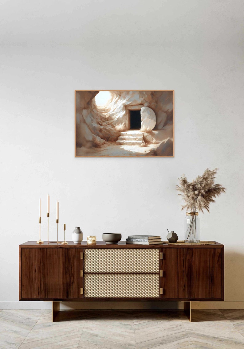 May include: A painting of a stone tomb with a large stone rolled away, revealing a dark opening. The tomb is lit by a bright light coming from the opening. The painting is framed in a light brown frame.