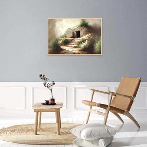 May include: A painting of a stone tomb with a large, round stone rolled away from the entrance. The tomb is set against a backdrop of a grassy hill and a cloudy sky. The painting is framed in a light wood frame.