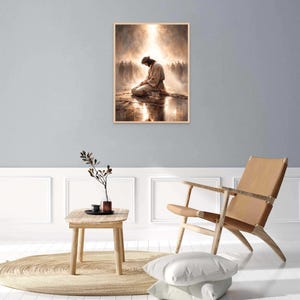 May include: A framed print depicts a figure kneeling in prayer, bathed in light. The artwork features a warm color palette with a soft, ethereal glow. The image is set against a backdrop of a crowd, with a reflective surface below the figure.
