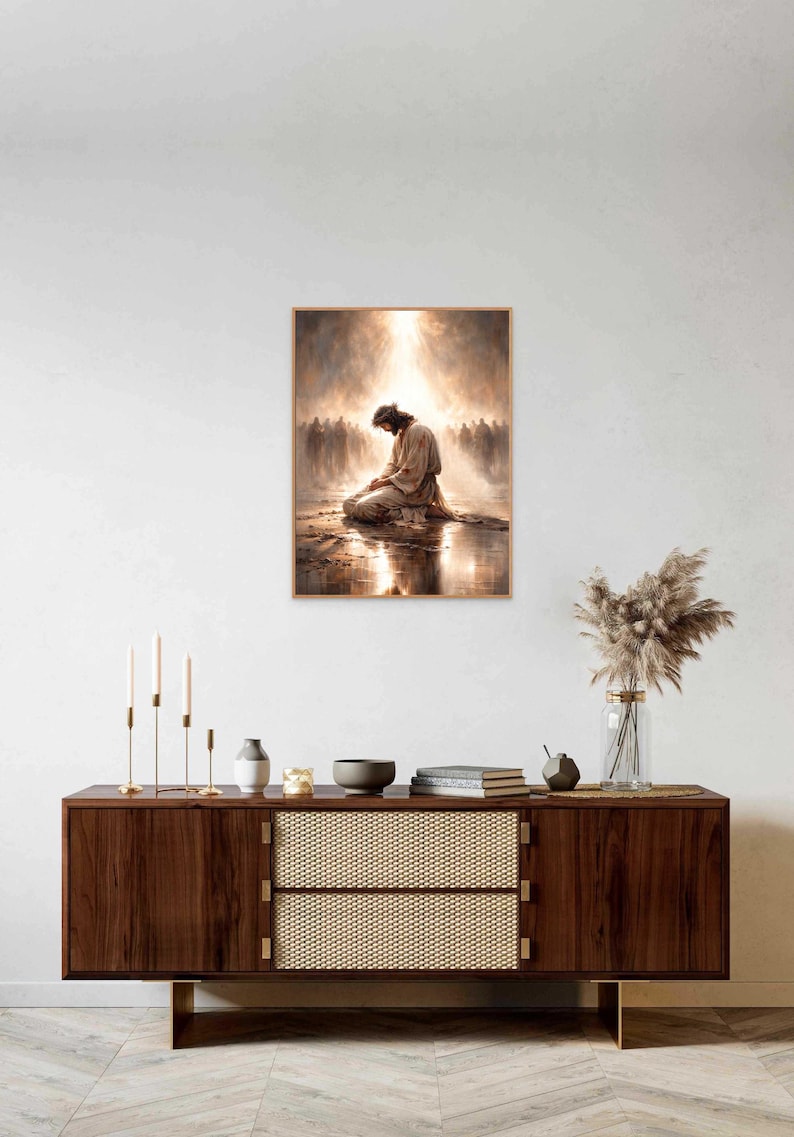 May include: A framed print depicts a figure kneeling in prayer, bathed in light, with a crowd in the background. The artwork has a warm color palette and is displayed above a wooden cabinet with decorative items.