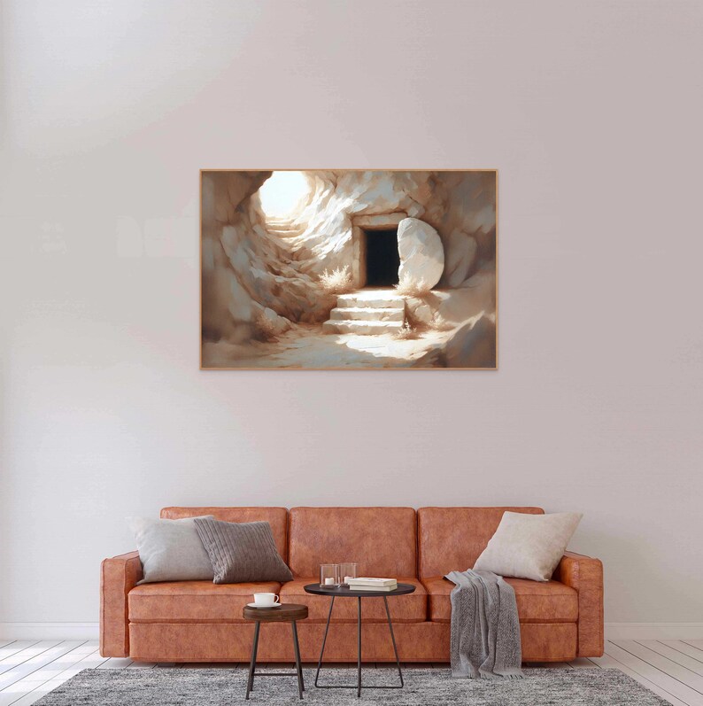 May include: A painting of a stone tomb with a large stone rolled away, revealing a doorway. The tomb is lit by a bright light coming from inside. The painting is framed and hanging on a wall above a brown leather couch.
