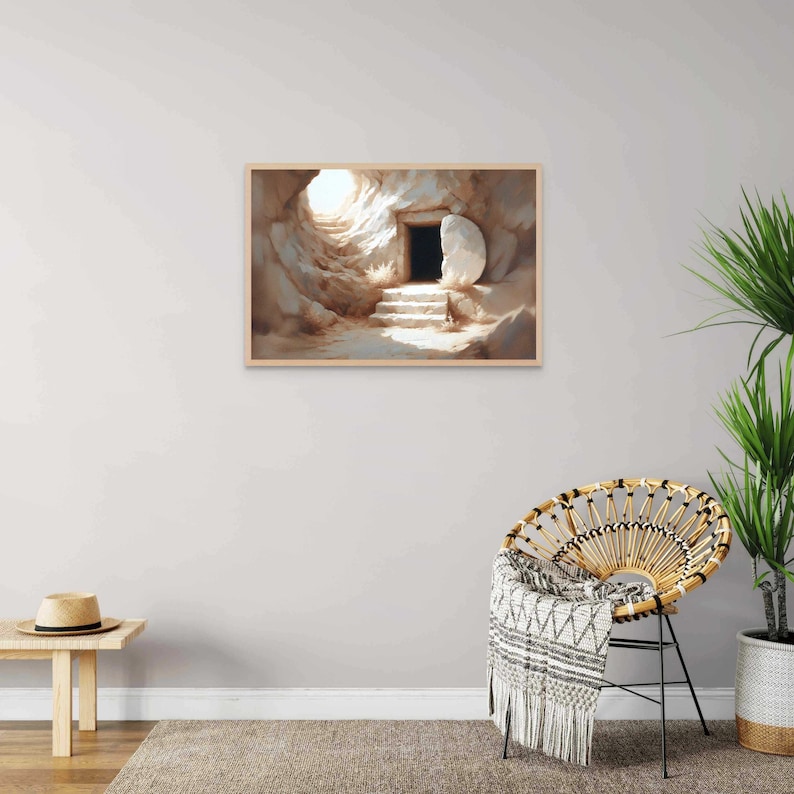 May include: A painting of a stone tomb with a large stone rolled away, revealing a dark doorway. Light shines from inside the tomb, illuminating the steps leading to the doorway. The painting is framed in a light wood frame.