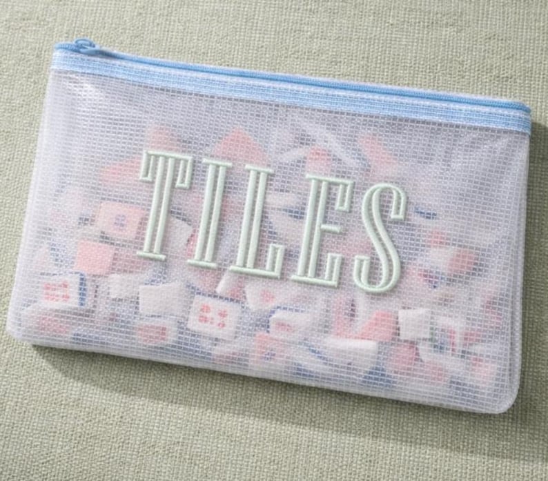 Puede incluir: Una bolsa con cremallera de malla transparente con la palabra "TILES" en letras verde claro. La bolsa est&aacute; llena de peque&ntilde;as baldosas cuadradas en tonos rosa, blanco y azul. La cremallera y el ribete son de color azul claro.