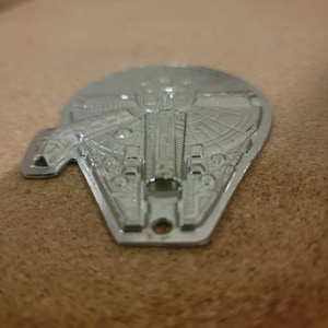 Pode incluir: Um chaveiro de metal prateado em forma da nave espacial Millennium Falcon de Star Wars.
